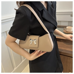 Detail of beige shoulder bag featuring a decorative silver bow buckle on the front flap