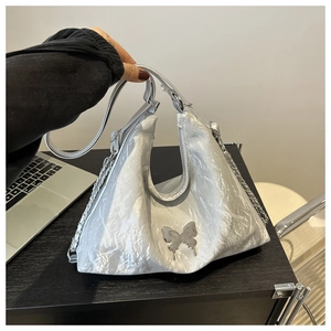 Détail du sac à bandoulière argenté plissé avec logo papillon en métal et chaîne décorative