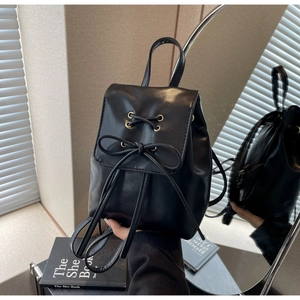 Detail showing mini black faux leather backpack with bow tie and metal ring accents