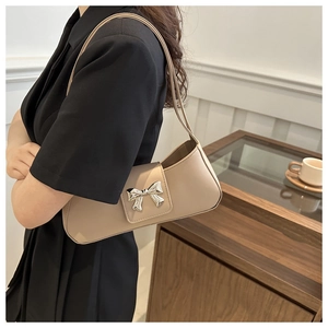 Detail of beige shoulder bag featuring a metallic silver bow clasp and magnetic flap cover