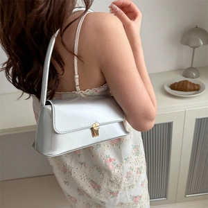 Sac sous le bras argenté minimaliste avec fermoir doré porté par un mannequin en décor élégant