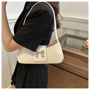 Detail of a creamy white shoulder bag featuring a silver bow-shaped magnetic buckle closure