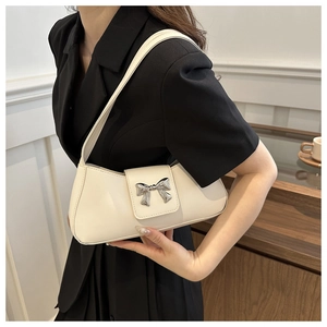 Detailed view of a creamy white underarm bag with a decorative silver metal bow charm
