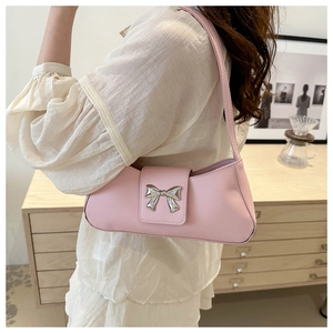 Detail shot of a pink bow shoulder bag worn by a model in a minimalist interior setting