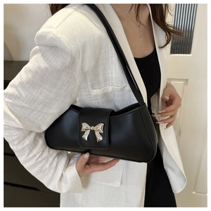 Detail of a black leather shoulder bag with a silver metal bow worn with a white blazer