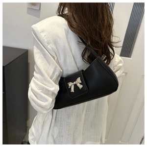 Detail of black leather underarm bag with a silver metal bow buckle on white clothing