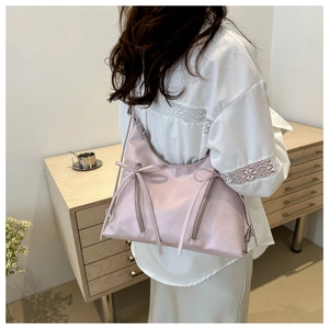 Detail of light pink shoulder bag featuring decorative vertical zippers and ribbon bow