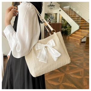 Détail d'un sac cabas en paille avec un grand nœud en satin blanc et anses en cuir