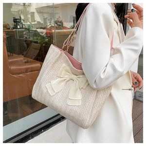 Détail d'un sac cabas en paille tressée avec un nœud en tulle et une bandoulière rose