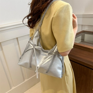 Silver metallic faux leather tote bag with stylish bows and zippers worn by a model