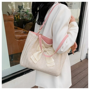 Détail d'un sac cabas en paille avec des anses en cuir rose et un grand nœud en soie crème