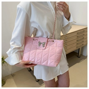 Detailed view of a pink quilted shoulder bag featuring a silver metal bow accent and chain strap