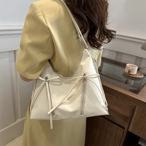 Minimalist beige tote bag with bow details and zippers shown on model's shoulder