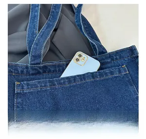 Detail of blue denim tote bag showing functional front pocket with yellow stitching