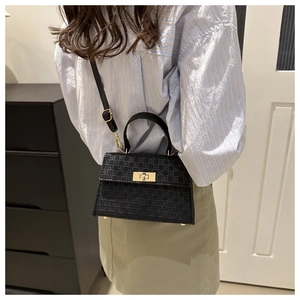 Rear view of a model wearing a black woven trapezoid crossbody bag with gold hardware