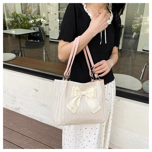 Détail d'un sac cabas en paille avec un grand nœud en satin crème et une bandoulière rose