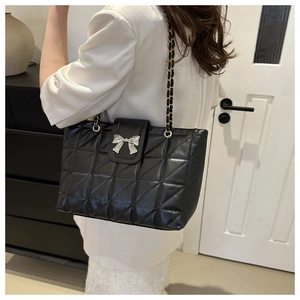Close-up of quilted black shoulder bag with silver bow detail and metal chain strap