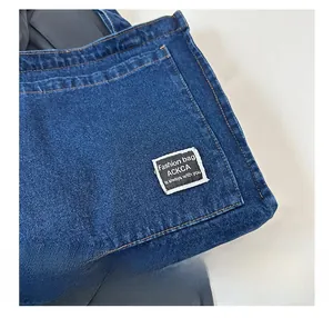 Close-up of dark blue denim tote bag featuring contrast stitching and brand logo tag