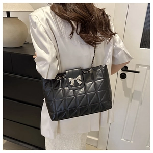 Close-up of black quilted shoulder bag with silver bow buckle and chain strap