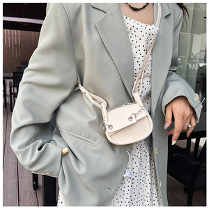 Detailansicht einer cremeweißen Satteltasche mit Silberkette und Leder-Schultergurt
