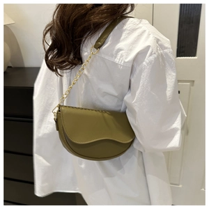 Close-up of olive green crescent saddle bag with gold metal chain on a model's shoulder