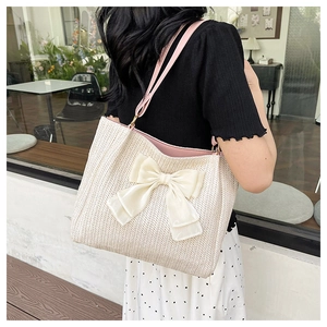 Détail du sac cabas en paille tissée avec grand nœud crème et bandoulière en cuir rose