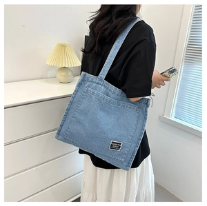 Detail of blue denim tote bag showing the front pocket and textured fabric finish