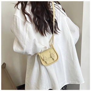 Petit sac bandoulière beige minimaliste à double boucle porté par un mannequin réel
