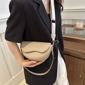 Minimalist beige saddle bag with wide knit strap and golden hardware shown on model