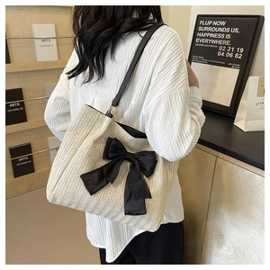 Détail du sac cabas en paille tissée avec un grand nœud noir et bandoulière en cuir