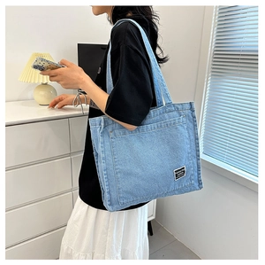 Detailed close-up of light blue denim tote bag featuring a black fashion logo label