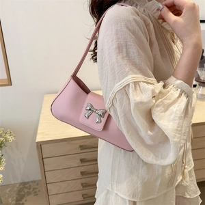 Pink matte leather shoulder bag with a silver bow, worn by a model in a warm room
