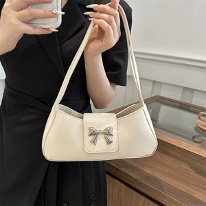 Elegant cream baguette bag with silver bow accent on a black dress backdrop