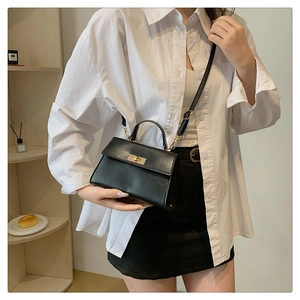 Detail view of black PU leather square handbag with golden rotating lock and crossbody strap