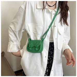 Petit sac bandoulière vert chic avec boucles décoratives porté par un mannequin