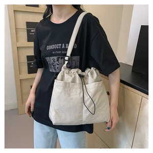 Detail view of beige nylon drawstring bucket bag with large dual pockets on shoulder strap