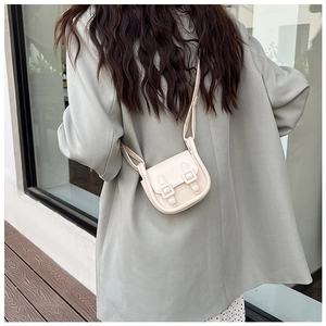 Vue détaillée d'un sac bandoulière crème porté sur un blazer gris par un mannequin