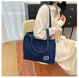Detail of a large dark blue denim tote bag with a white woven label for daily commuting