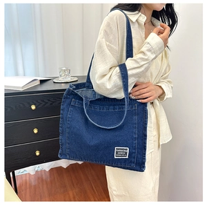 Detail of blue denim tote bag showing the white label and contrast stitching accents