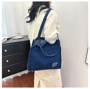 Detail view of large dark blue denim tote bag with white fashion label and shoulder straps