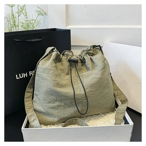 Close-up of a sage green nylon drawstring crossbody bag in a gift box with a shopping bag
