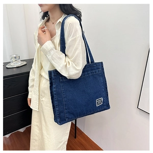 Detail of deep blue denim tote bag worn over shoulder with elegant white logo patch