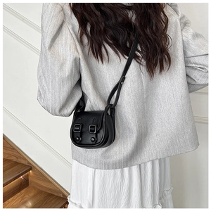 Détail d'un sac bandoulière vintage noir avec rabat et boucles décoratives sur des escaliers