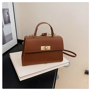 Close-up of brown faux leather crossbody bag with golden rectangular clasp on books