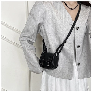 Détail d'un mini sac bandoulière noir mat porté avec un blazer gris et une jupe plissée