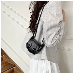 Petit sac besace noir avec double boucles porté par un mannequin en costume gris