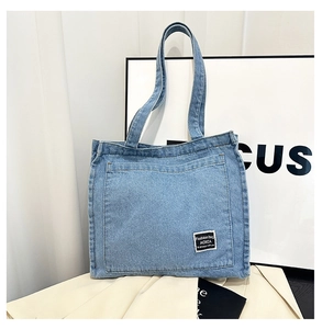 Detail of light blue denim tote bag showing the front pocket and woven fashion label