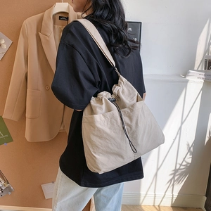 Minimalist beige drawstring crossbody bucket bag with wide shoulder strap in natural sunlight