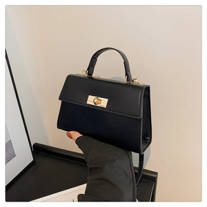Detail view of a black matte leather crossbody bag with a golden metal twist lock and handle