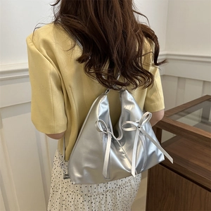 Sac hobo argenté chic avec nœuds latéraux présenté sur l'épaule d'un mannequin